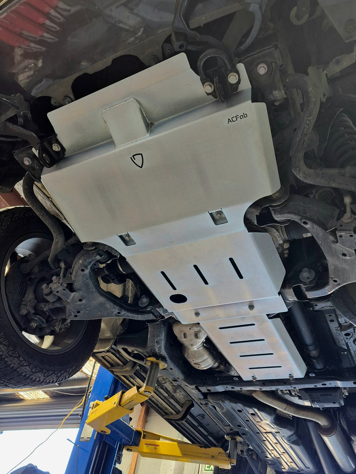 Angled front underside view of Landcruiser 300 bash plates showing shield logo and raised front section
