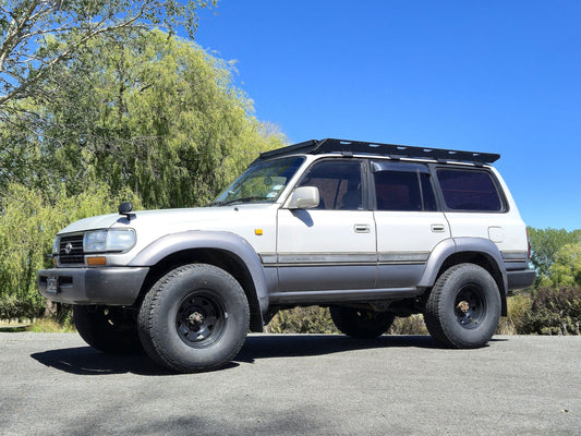 Silver Toyota Landcruiser 80 series with full-length black roof rack, low front-side view